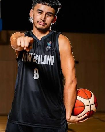 A player in a New Zealand number 8 singlet points towards the camera while holding a basketball.