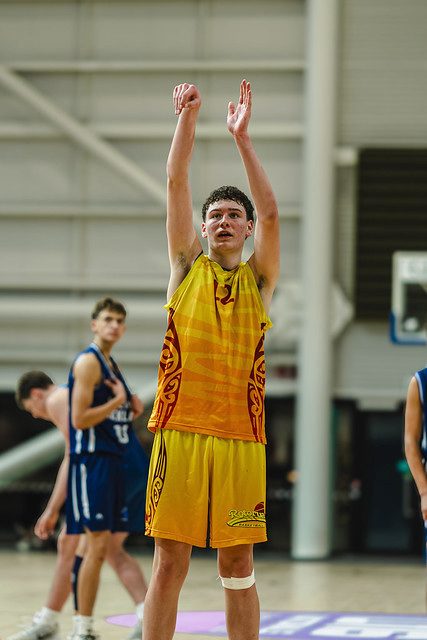 Rotorua player holds his shooting follow-through with both arms raised.