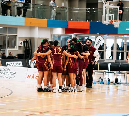 Rotorua players and staff gather in a close team huddle on court.