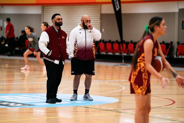 Two team staff members watch the court while a player holds the ball nearby.